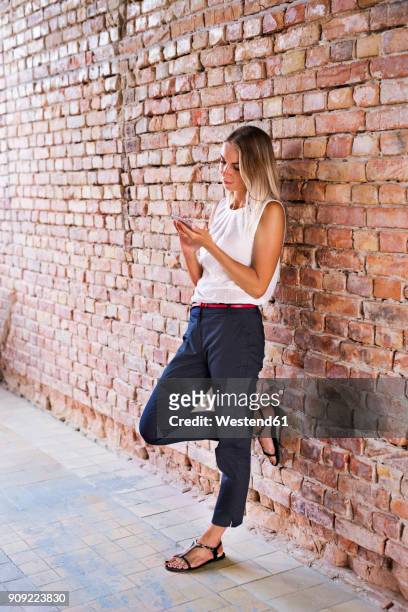 businesswoman using cell phone at brick wall - leaning stock pictures, royalty-free photos & images