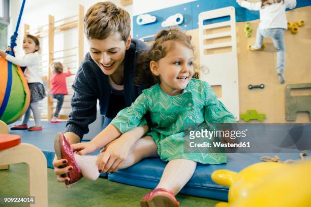 pre-school teacher helping little girl putting a shoe on - nursery school building stock pictures, royalty-free photos & images