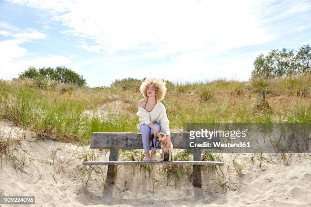 young woman sitting on bench in the dunes with her dog looking at distance - travemuende stock pictures, royalty-free photos & images