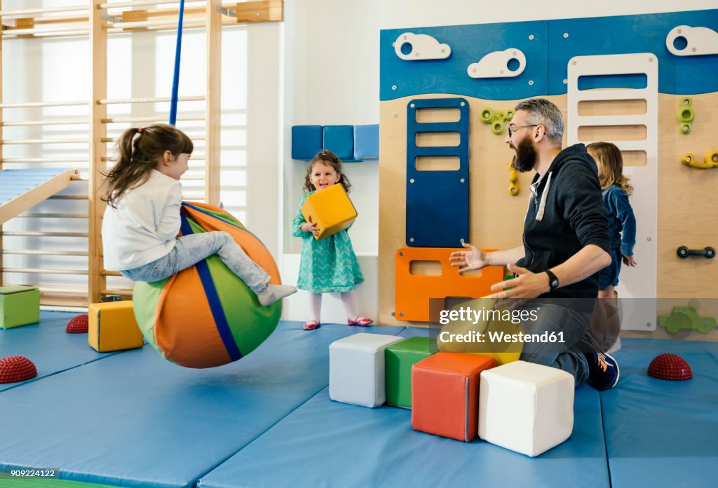 Pre-school teacher and happy children playing in gym room in kindergarten