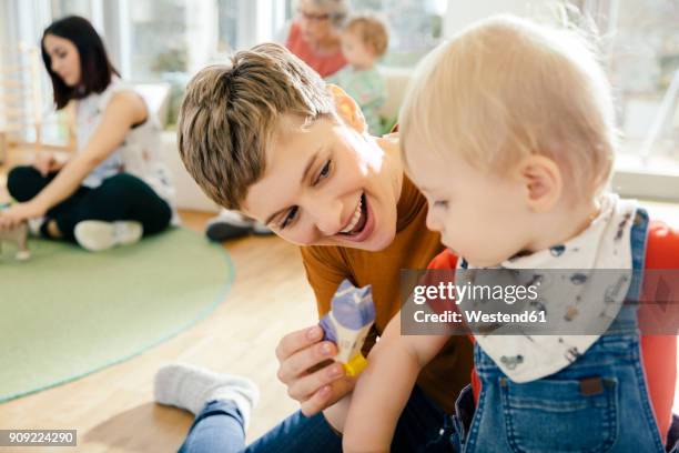 pre-school teacher playing with toddler in kindergarten - kindergartengebäude stock-fotos und bilder