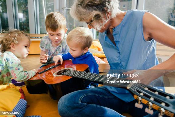 pre-school teacher showing a guitar to children in kindergarten - kindergartengebäude stock-fotos und bilder