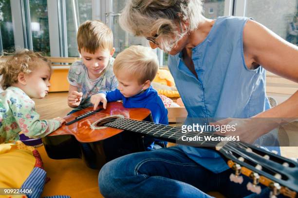 pre-school teacher showing a guitar to children in kindergarten - toddler musical instrument stock pictures, royalty-free photos & images