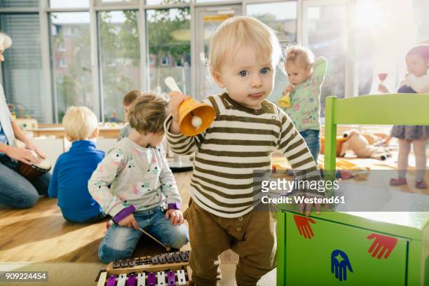 toddler ringing a bell in music room of a kindergarten - peuterschool stockfoto's en -beelden