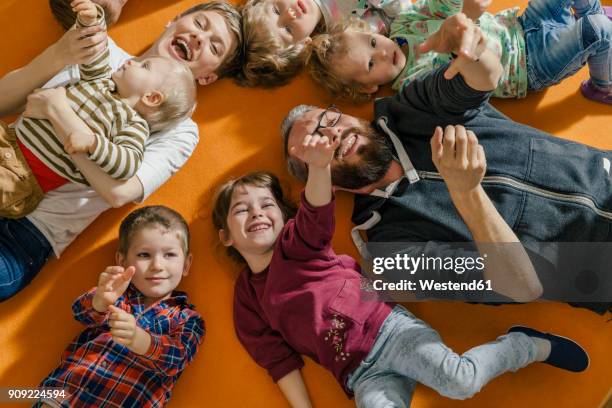 children and teachers lying and singing on carpet in kindergarten - kindergartengebäude stock-fotos und bilder