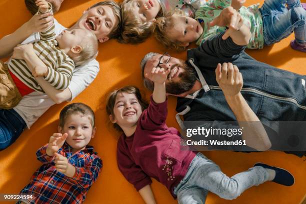 children and teachers lying and singing on carpet in kindergarten - nursery school building stock pictures, royalty-free photos & images