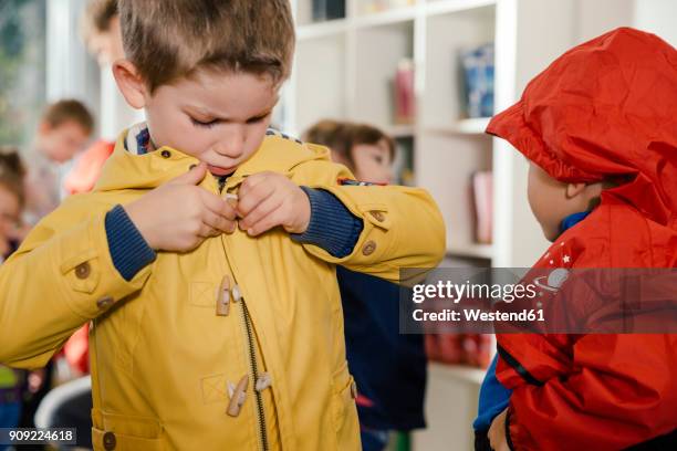 boy putting on his raincoat in kindergarten - girl oilskin stock pictures, royalty-free photos & images