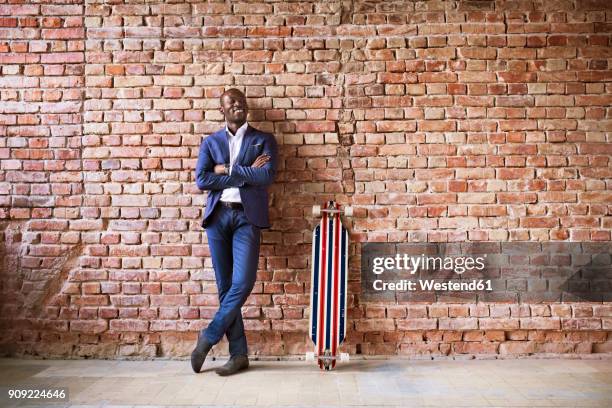 smiling businessman with longboard at brick wall - leunen stockfoto's en -beelden