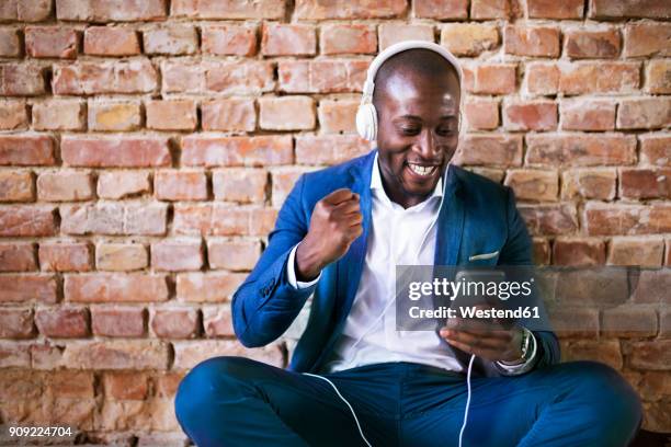 happy businessman with headphones and smartphone cheering - siegerpose stock-fotos und bilder