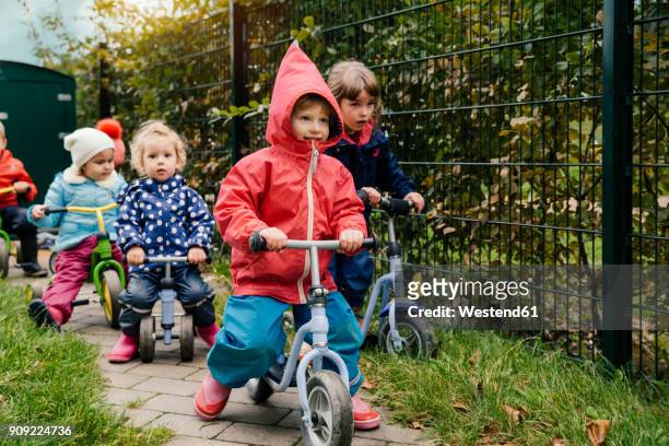 children using scooters in garden of a kindergarten - rain coat stock pictures, royalty-free photos & images