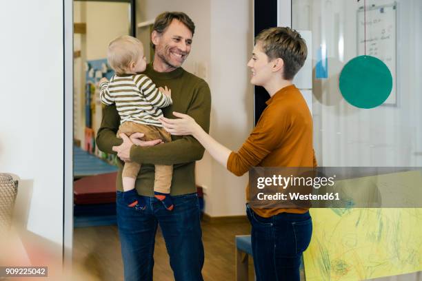 pre-school teacher talking to father with toddler in kindergarten - kindergartengebäude stock-fotos und bilder