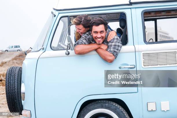 spain, tenerife, portrait of laughing man and his girlfriend leaning out of car window of camper - auto blau stock-fotos und bilder