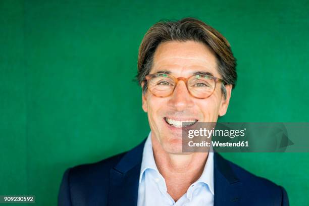 portrait of smiling businessman with glasses in front of green wall - green suit stock-fotos und bilder