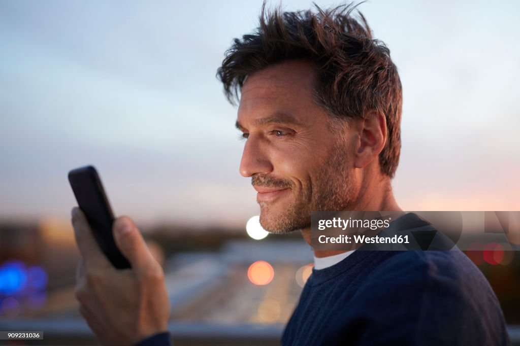 Smiling man in the city checking cell phone in the evening