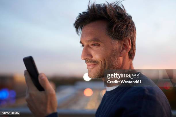 smiling man in the city checking cell phone in the evening - sehen stock-fotos und bilder