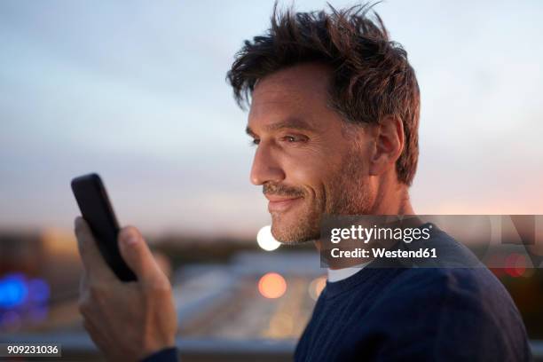 smiling man in the city checking cell phone in the evening - mobile foto e immagini stock