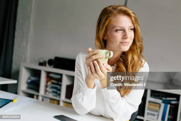 smiling young woman with cup of coffee at desk in office - founders cup portraits fotografías e imágenes de stock