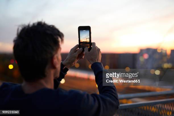 man in the city taking cell phone picture in the evening - take pictures stock-fotos und bilder