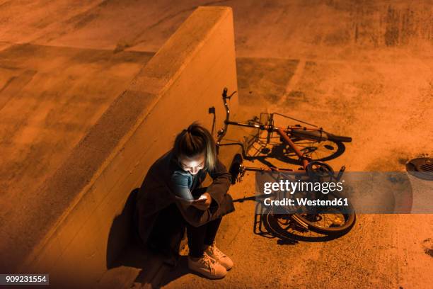 young woman in the city checking cell phone at night - fahrrad nacht stock-fotos und bilder