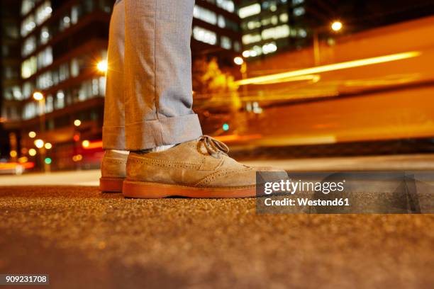 feet of businessman standing at roadside in the city at night, close-up - suede shoe stock-fotos und bilder