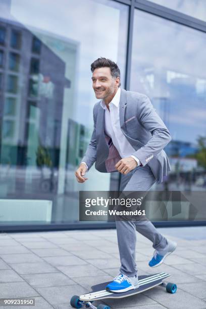 portrait of smiling businessman skateboarding on pavement - agilität stock-fotos und bilder