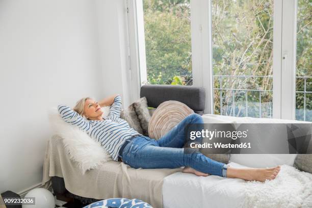 smiling senior woman relaxing on couch in the living room - op de rug liggen stockfoto's en -beelden