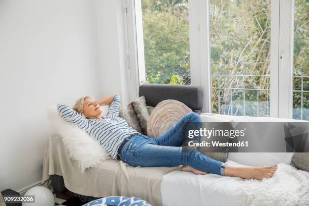 smiling senior woman relaxing on couch in the living room - reclining stockfoto's en -beelden