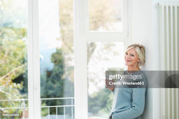 portrait of senior woman with glass of water in front of window - drinking water glass woman stock-fotos und bilder