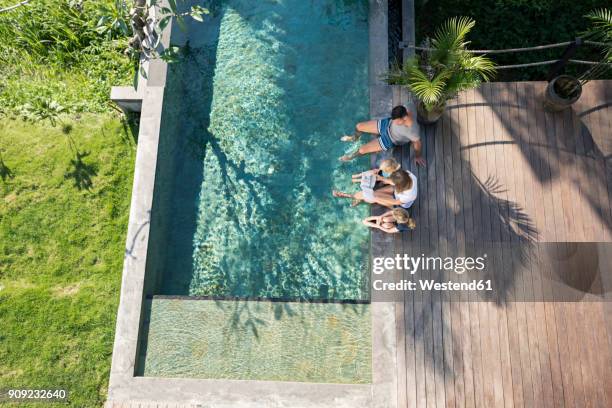 family sitting at the swimming pool, mother reading book for children - bali luxury stock pictures, royalty-free photos & images