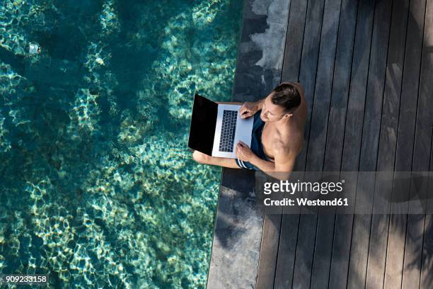mature man sitting at the poolside, using laptop - time off work stock pictures, royalty-free photos & images