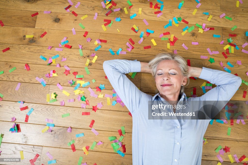 Portrait of smiling senior woman lying on floor covered with confetti