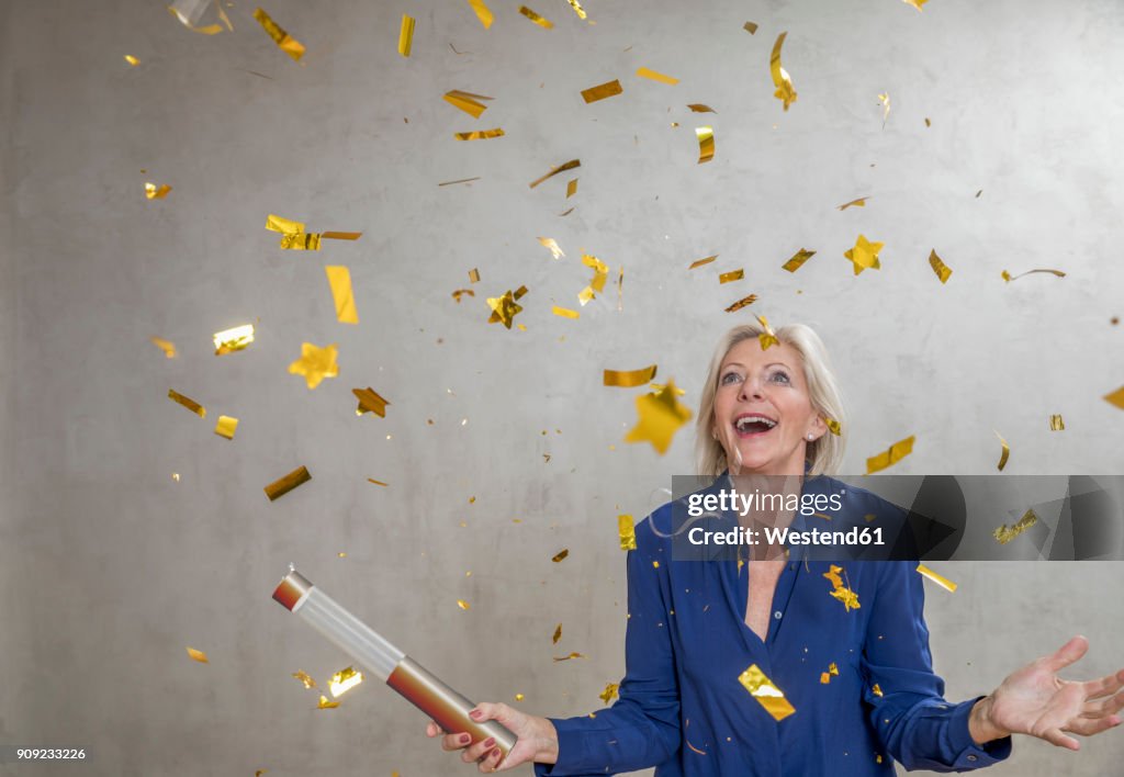 Portrait of amazed senior woman watching golden confetti
