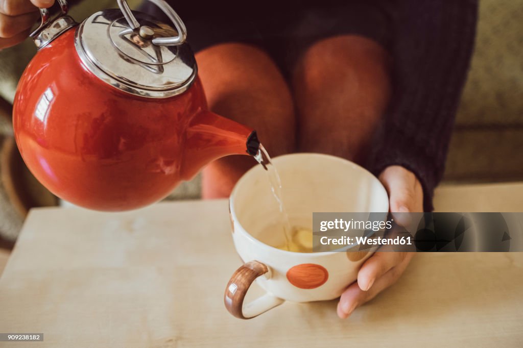 Woman pouring water into tea cup with chopped fresh ginger, close-up