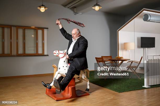 businessman on rocking horse pretending to ride - bizzarro foto e immagini stock