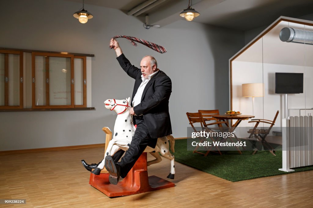 Businessman on rocking horse pretending to ride