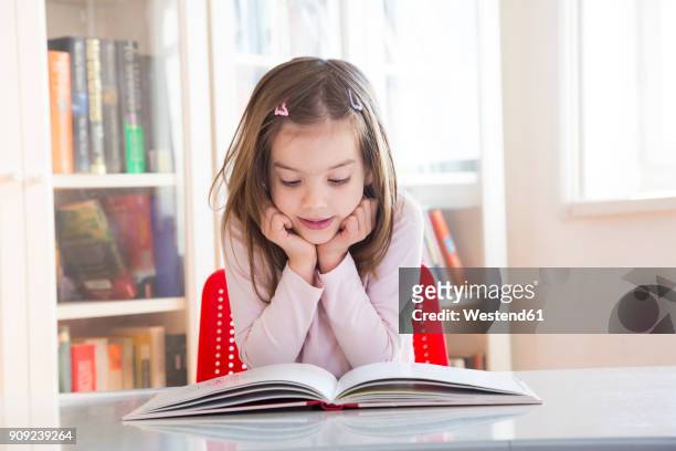 portrait of little girl at table reading a book - day 6 stock-fotos und bilder