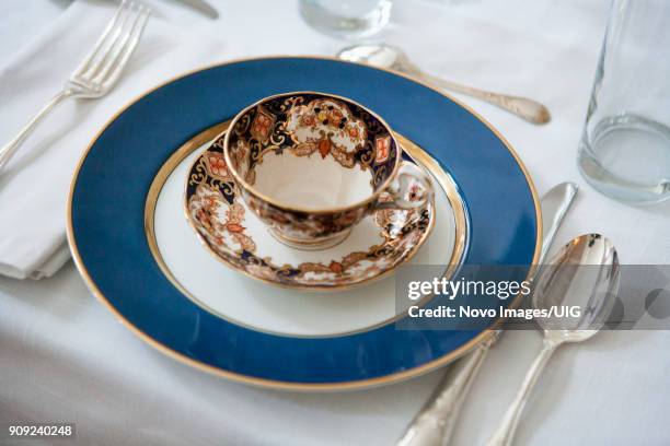 formal dining table setting with blue-accented teacup and saucer on plate with silverware - formal dining stock pictures, royalty-free photos & images