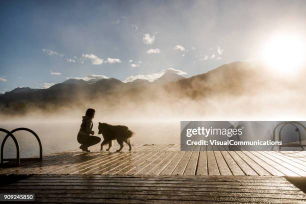 young woman and dog watching sunrise by the lake. - watching sunrise stock pictures, royalty-free photos & images