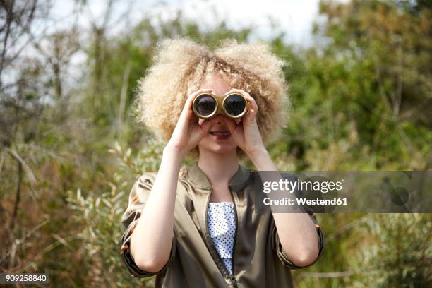 young woman with curly hair looking through old binoculars - binoculars stock pictures, royalty-free photos & images