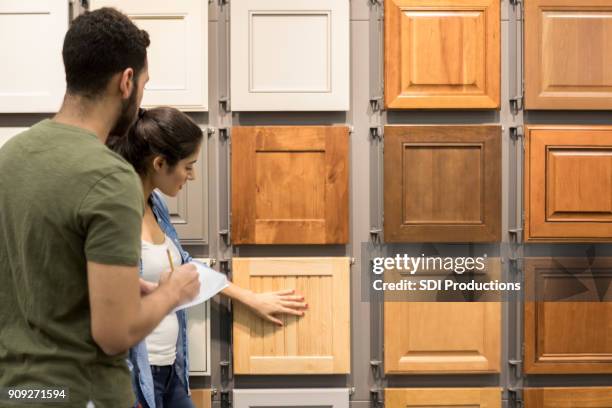 young couple look at cabinet samples in home improvement store - wood furniture stock pictures, royalty-free photos & images