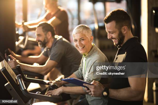 glückliche senior frau spaß mit ihrer trainerin auf spinning-klasse in ein fitness-studio. - gym images stock-fotos und bilder