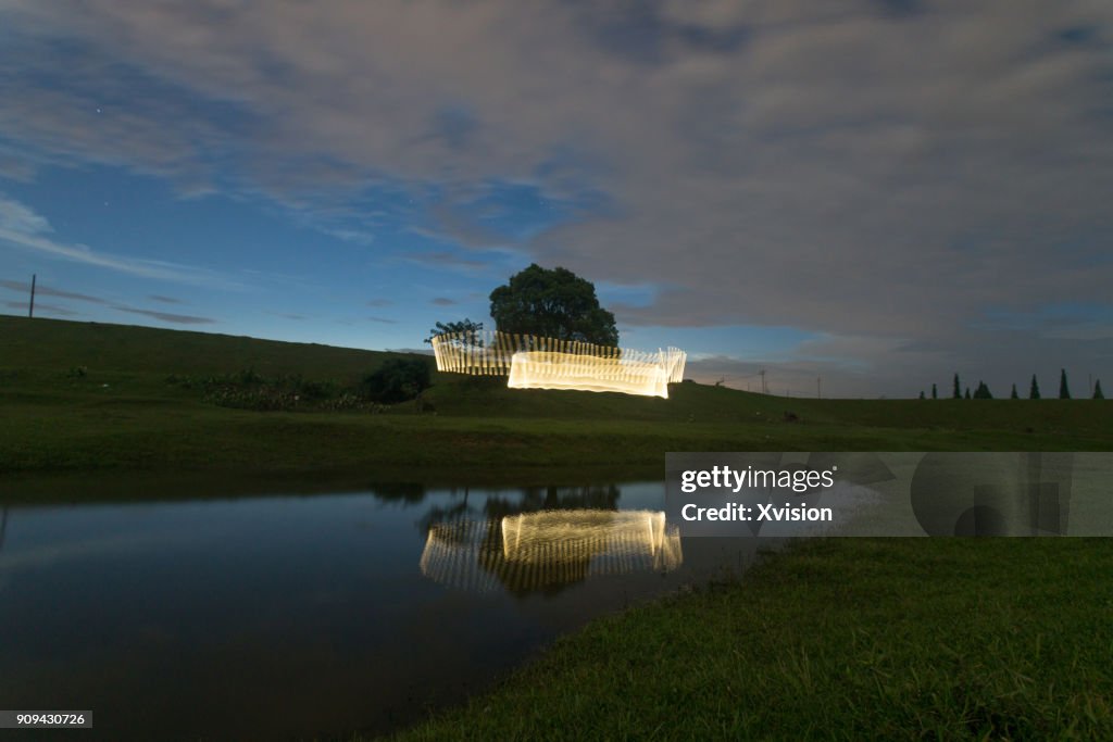 Light painting over a pond with a big tree behand in the grass field