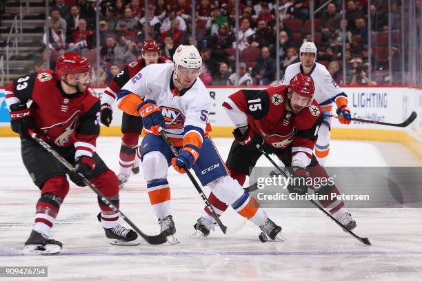 Ross Johnston of the New York Islanders skates with the puck between Alex Goligoski and Brad Richardson of the Arizona Coyotes during the NHL game at...