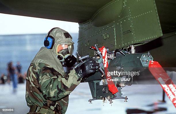 An airman wearing biological-chemical protective gear makes an adjustment to a bomb rack mounted on an A-10 Thunderbolt aircraft during the combat...