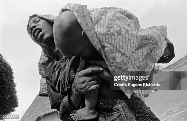 Low-angle view of an unidentified woman, blind after suffering from measles, as she holds her young daughter in her arms, Niamey, Niger, 1994. The...