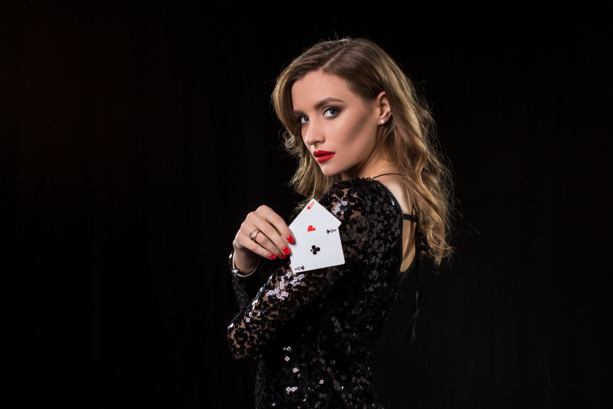 Young woman holding playing cards against a black background Young woman holding playing cards against a black background