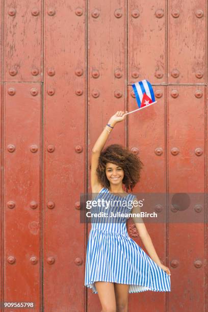 pretty cuban woman standing with cuban flag against red door - havana door stock pictures, royalty-free photos & images