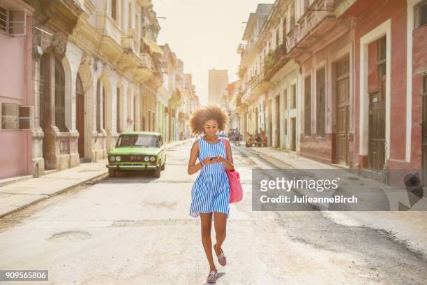 cubaanse meisje kijkend naar mobiele telefoon, lopend onderaan de straat in havana - havana stockfoto's en -beelden
