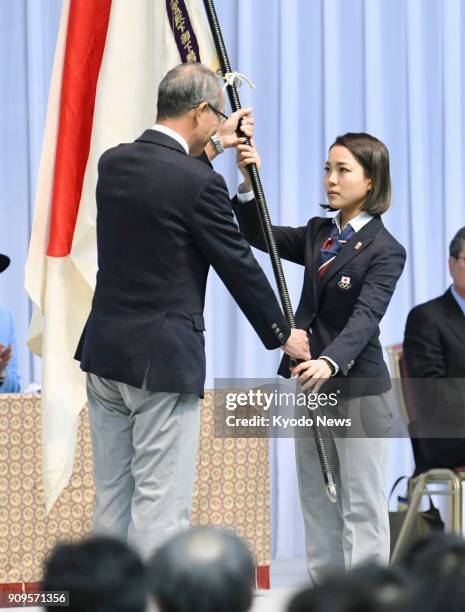 Ski jumper Sara Takanashi receives the Japan flag from Yasuo Saito, one of the vice presidents of the Japanese Olympic Committee, during an...