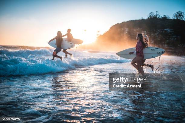 amigos corriendo en el océano con sus tablas de surf - entrando fotografías e imágenes de stock